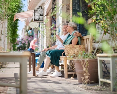 Ein Paar sitzt mit Kompressionsstrümpfen auf einer Bank bei schönem Wetter.